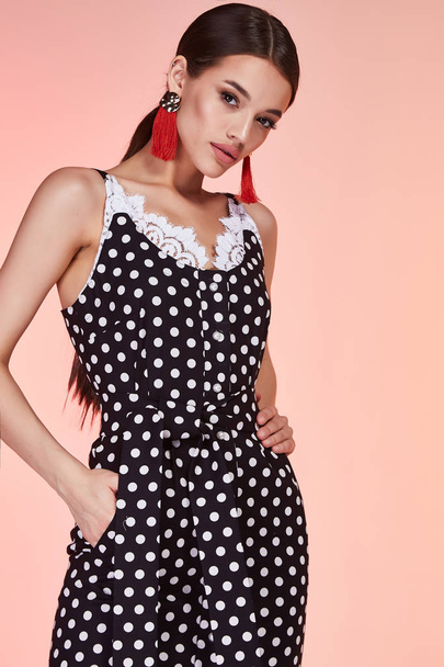 Beautiful sexy woman pretty face long brunette hair wear black polka dot skinny dress fashion style clothes for business woman office casual walk summer collection jewelry earrings glamour model pose. - Fotó, kép