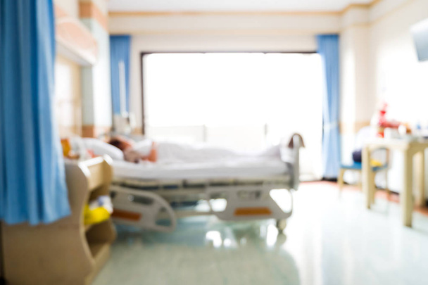 Blurred background of patient lying on bed in hospital room with nature light from window. Blurry image of recovery room with bed and comfortable medical equipped for patient for background. - Fotó, kép