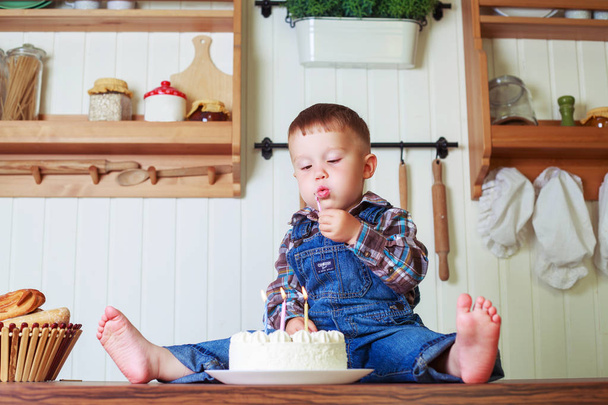 Baby thuis in de keuken met een grote taart met kaarsen - Foto, afbeelding