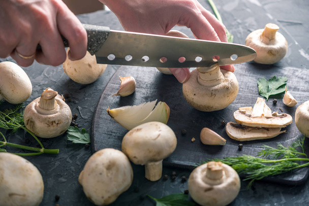 Le mani delle donne stanno tagliando champignons con un coltello sul tavolo della cucina scura. Il concetto di cucinare piatti a base di funghi. Da vicino.
 - Foto, immagini