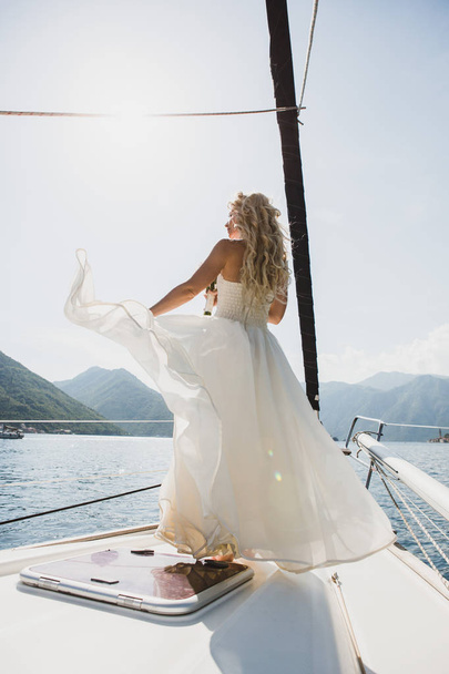 Beautiful stylish bride in a white wedding dress on luxury yacht sailing down the sea on wedding day - 写真・画像