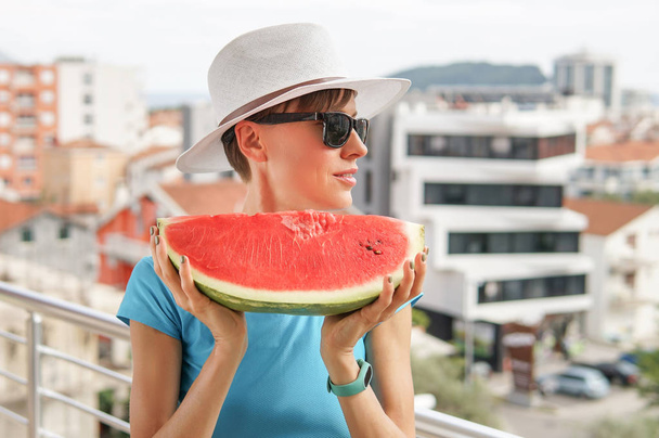 Portrait happy young woman is holding slice of watermelon over over city background - Фото, изображение