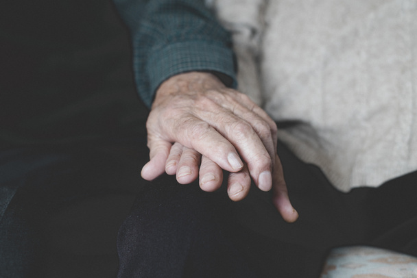 Close-up van een oude blanke man en een oude blanke vrouw zittend in een bank hand in hand met genegenheid - Foto, afbeelding