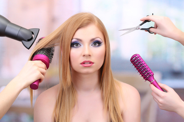 Beautiful woman and hands with brushes, scissors and hairdryer in beauty salon - Photo, image