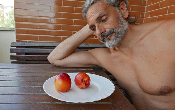 hombre maduro sin camisa comiendo frutas frescas de melocotón
 - Foto, Imagen
