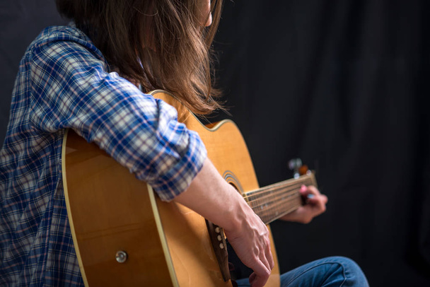 A lány tinédzser játszik akusztikus gitár, sötét háttér előtt a stúdióban. Koncerten fiatal zenészek - Fotó, kép