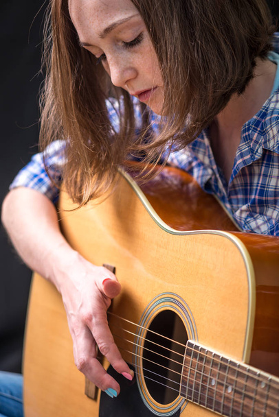 A adolescente tocando uma guitarra acústica em um fundo escuro no estúdio. Concerto de jovens músicos
 - Foto, Imagem