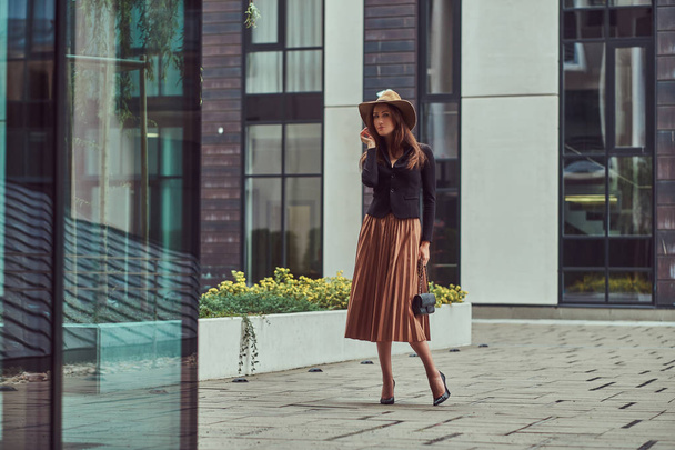 ヨーロッパの都市の中心部を歩いてクラッチ バッグと黒のジャケット、茶色の帽子、スカートを着てファッション エレガントな女性. - 写真・画像