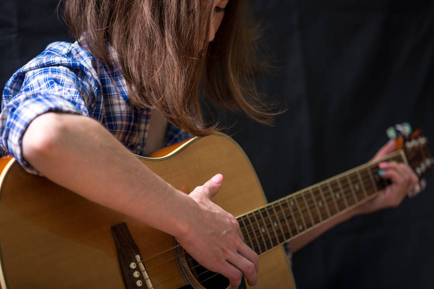 La chica adolescente tocando una guitarra acústica sobre un fondo oscuro en el estudio. Concierto de jóvenes músicos
 - Foto, imagen