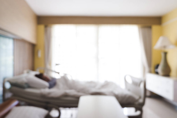 Blurred background of patient lying on bed in hospital room with nature light from window. Blurry image of recovery room with bed and comfortable medical equipped for patient for background. - Foto, Imagen