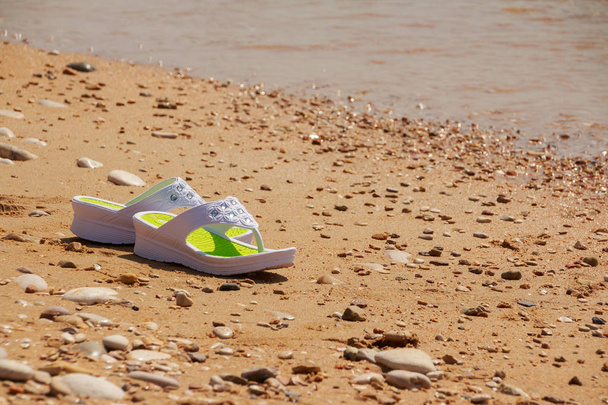 bílé sandály na pláži. Na písčité mořské pláži - letní dovolená koncepce flipflops. Pláž móda. Dámské letní boty pro volný čas. Kopírovat prostor - Fotografie, Obrázek