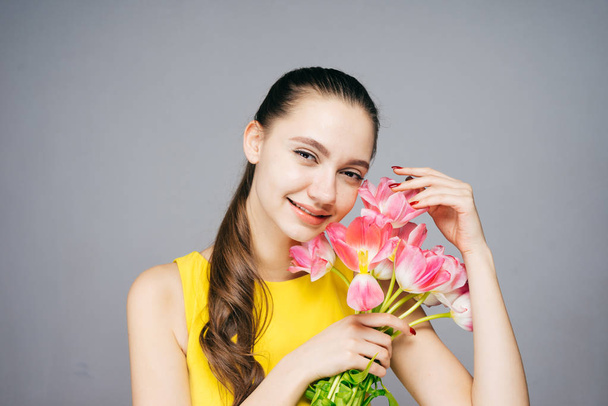 attractive smiling woman in yellow dress holds fragrant pink flowers and poses - Foto, Bild
