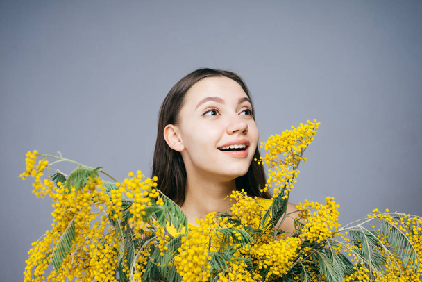 beautiful young girl holding an aromatic yellow mimosa, smiling and enjoying the spring - Photo, image