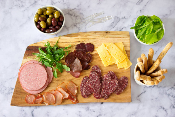 Appetizer table for wine or beer with sausages, dried meat and cheese, served with grissini, herbs and olives. Selective focus. - Φωτογραφία, εικόνα