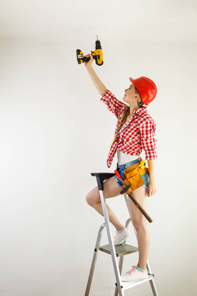 Mladá odhodlaná žena používá vrtačku na renovaci domu. Žena stavební dělnice s vrtačkou nástroje vrtné stěny. - Fotografie, Obrázek
