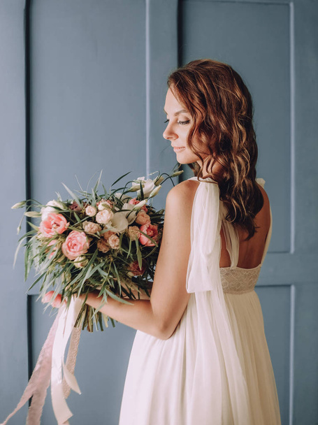 young beautiful girl in a chic dress with a bouquet of flowers on the background of a textured wall - Foto, Imagem