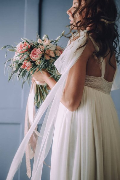 young beautiful girl in a chic dress with a bouquet of flowers on the background of a textured wall - Photo, image