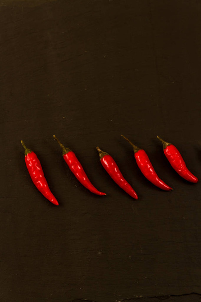 Row of seven red chillies with copyspace, black background, dark. - Photo, Image