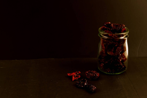 Low lit, with copy space, black area with sun dried tomatoes in jar and on surface. - Foto, Imagem