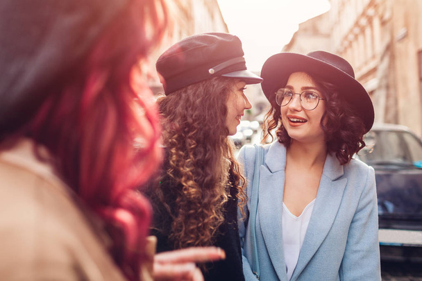 Outdoor shot of three stylish young women talking on city street. Happy girlfriends chatting and having fun - Photo, Image