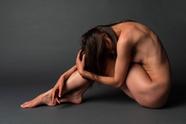 Tall slender Ukrainian brunette sitting nude on a gray background - Photo, Image