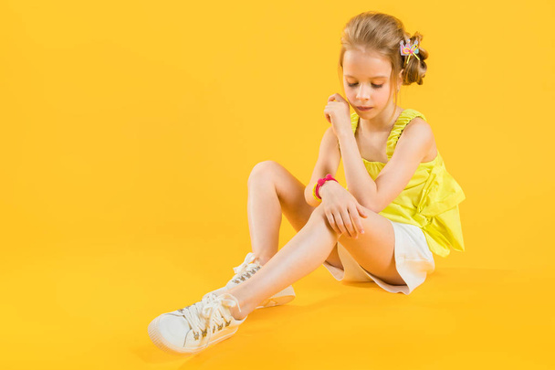 Μια έφηβη κοπέλα κάθεται σε κίτρινο φόντο. - Φωτογραφία, εικόνα