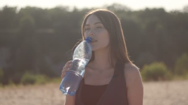 Fiatal nő utas ivóvíz egy műanyag üveg a természetben, a forró homokos területen. Lány érzés szomjúság a víz szünetet a naplemente - Felvétel, videó