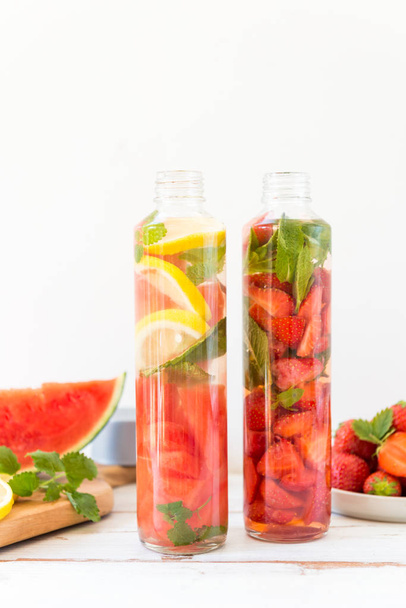 Detox Water doordrenkt met fruit en bessen binnen. Een met citroen, watermeloen en Mint, anderzijds een is met aardbeien en munt. Sport flessen, gezonde levensstijl concept - Foto, afbeelding