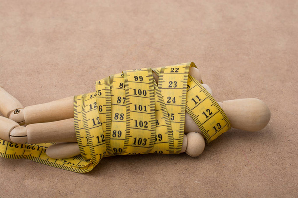 Yellow color measuring tape wrapped on wooden man - Photo, Image