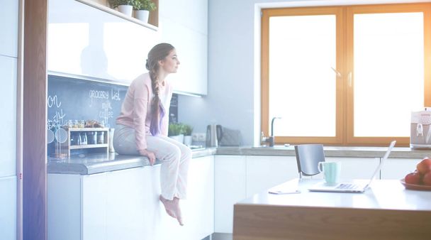 Young woman sitting on table in the kitchen. - Foto, Bild