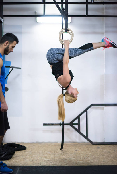 young athletic woman working out with personal trainer on gymnastic rings at the cross fitness gym - Foto, Imagem