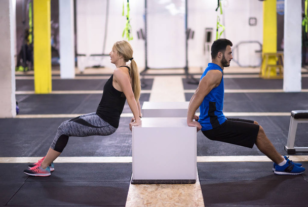 young couple athletes working out their arms using boxes at cross fitness gym - Photo, Image