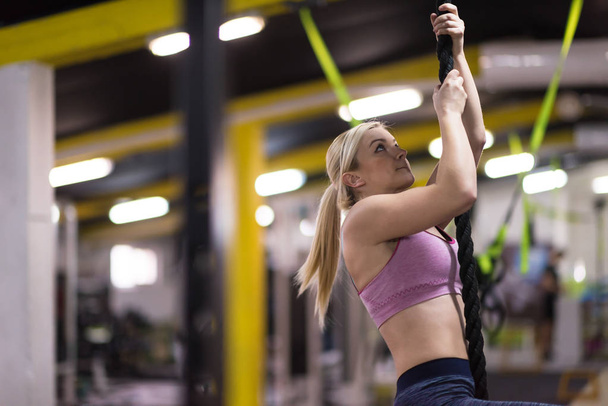 young muscular woman doing rope climbing in cross fitness gym - Foto, Imagem