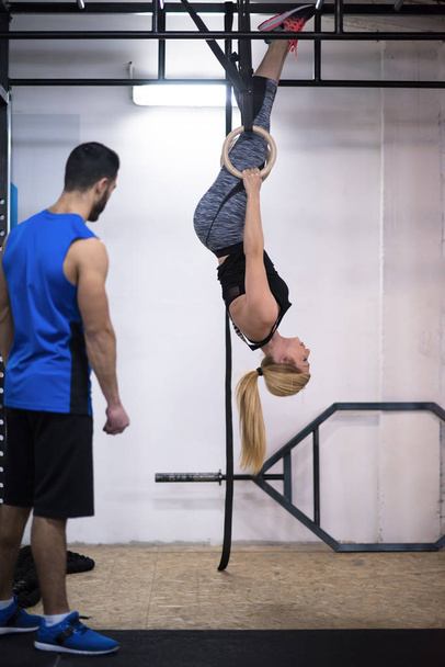young athletic woman working out with personal trainer on gymnastic rings at the cross fitness gym - Valokuva, kuva