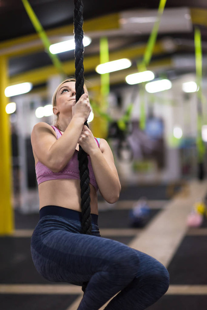 young muscular woman doing rope climbing in cross fitness gym - Photo, Image