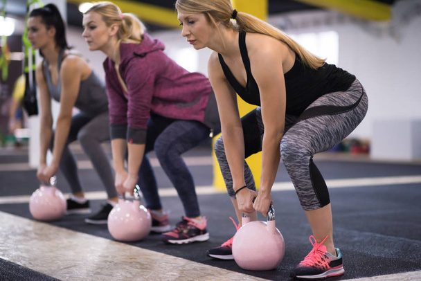group of healthy young athletes doing exercises with kettlebells at cross fitness studio - Foto, afbeelding