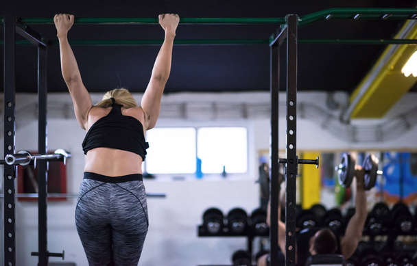 athlete woman doing abs exercises hanging upside down on horizontal bar at cross fitness gym - Fotó, kép