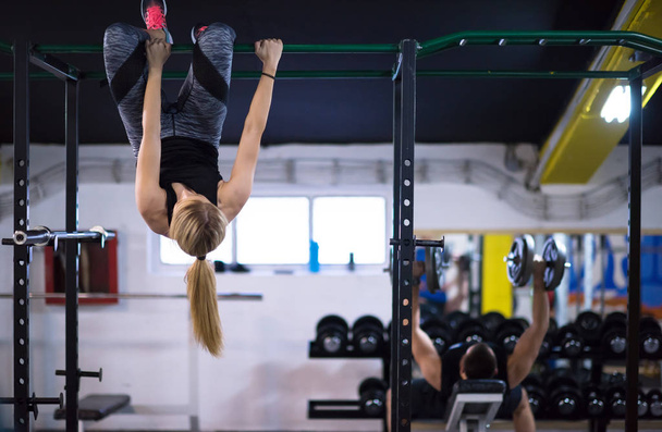 athlete woman doing abs exercises hanging upside down on horizontal bar at cross fitness gym - Фото, изображение