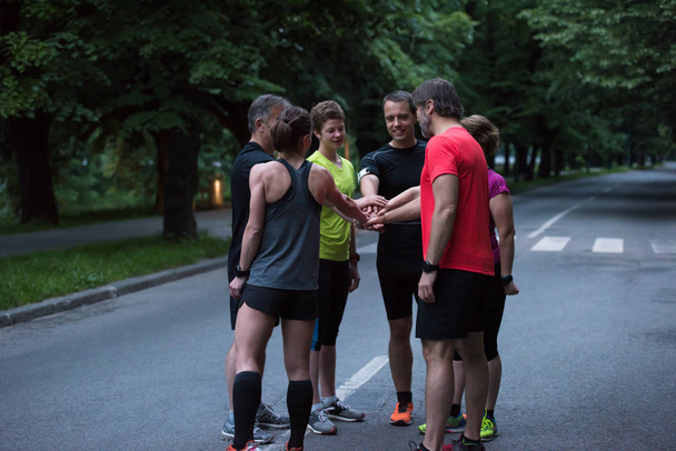 Skupina zdravých běžců dává plácnutí na sebe při oslavě úspěchu po tréninku. - Fotografie, Obrázek
