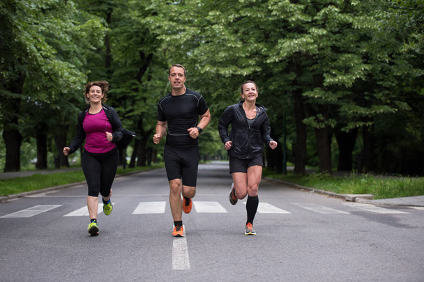 группа здоровых людей бег трусцой в городском парке, команда бегунов на утренней тренировке - Фото, изображение