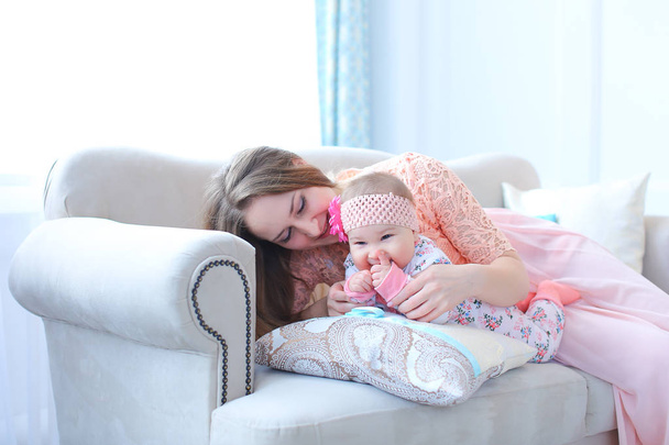 Młody bardzo matka siedzi z dzieckiem na kanapie i sukience różowy. - Zdjęcie, obraz