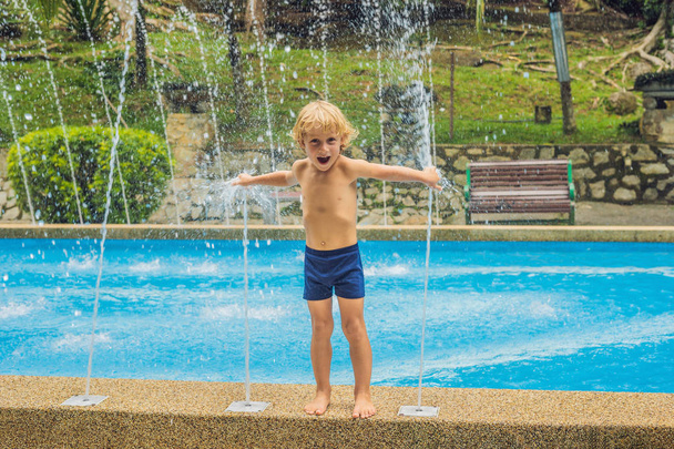 Menino feliz brincando com fonte de água na piscina
 - Foto, Imagem
