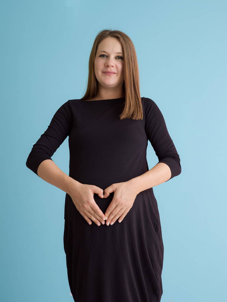 Boldog terhes nő hasa alatt kék háttér elszigetelt kezével portréja - Fotó, kép