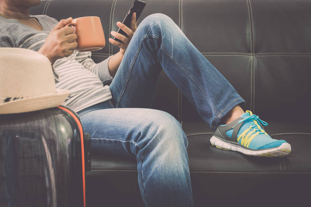 Femme voyageur est relaxant sur canapé en cuir tenant téléphone portable et tasse de café avec sac de voyage à l'aéroport.Concept de voyage
. - Photo, image