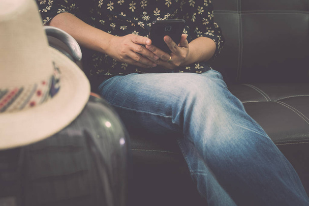 Жінка-мандрівник розслабляється на шкіряному дивані, що тримає мобільний телефон в аеропорту. Концепція подорожей
. - Фото, зображення