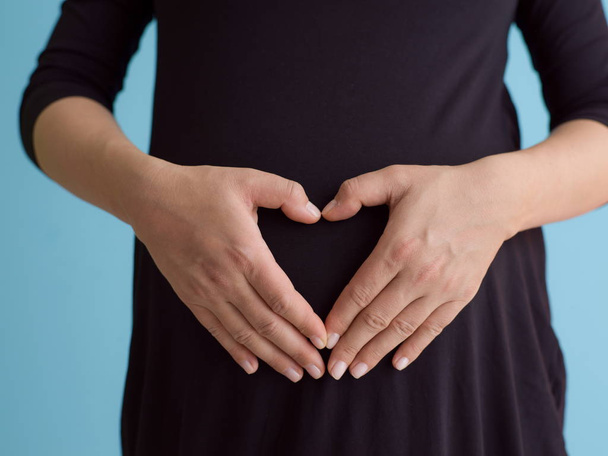 Portrait of happy pregnant woman with hands on belly isolated over blue background - Φωτογραφία, εικόνα