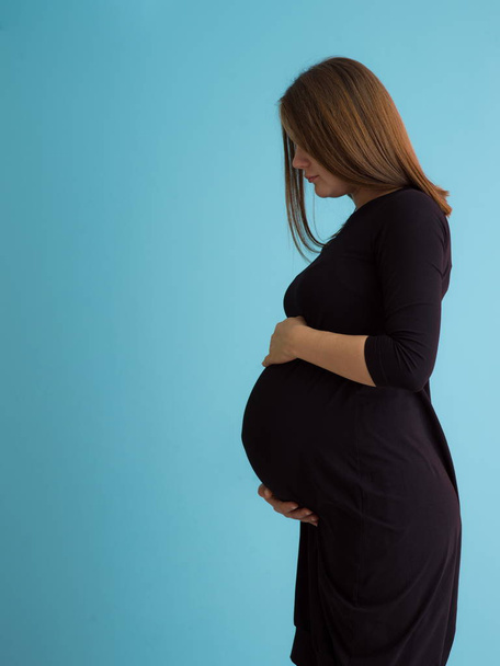 Portrait of happy pregnant woman with hands on belly isolated over blue background - Foto, imagen