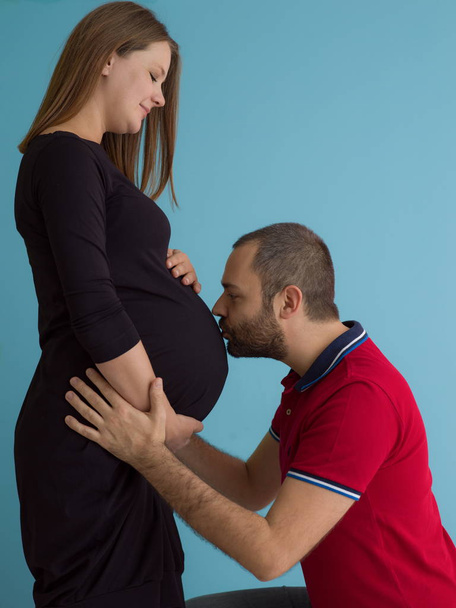 Portrait of a happy young couple,man holding his pregnant wife belly isolated over blue background - Foto, Bild