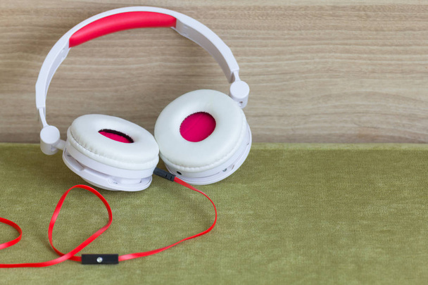 A big white and red headphones on green sofa, with wooden wall background. - Photo, Image