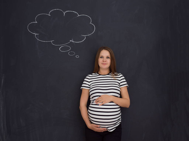 young pregnant woman thinking about names for her unborn baby to writing them on a black chalkboard - Foto, Bild